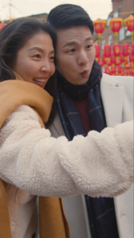 Video-Vertical-De-Una-Joven-Pareja-Asiática-De-Vacaciones-Posando-Para-Una-Selfie-En-Un-Teléfono-Móvil-En-Chinatown,-Londres,-Reino-Unido-1